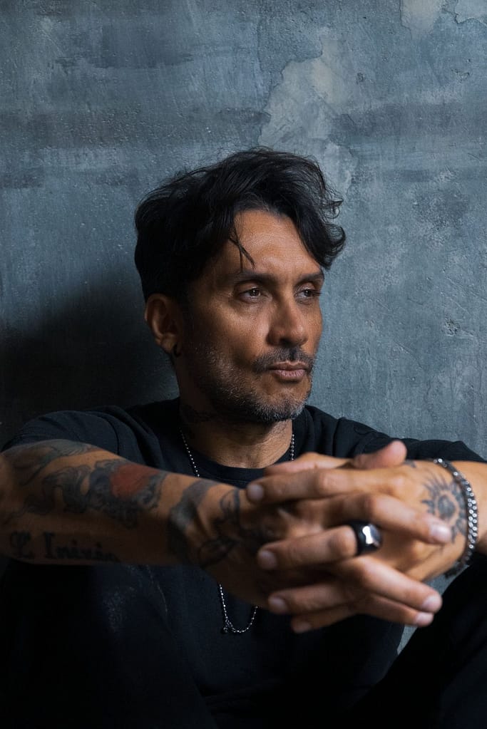 Ritratto di Fabrizio Moro seduto contro un muro grigio